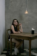 Serious Hispanic woman sitting at wooden table in corner