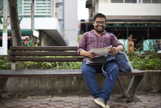Hispanic man sitting on bench reading brochure