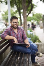 Smiling Hispanic man sitting on bench reading brochure