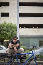 Smiling Hispanic man sitting on bench with bicycle