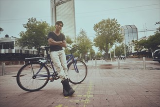 Smiling Hispanic man leaning on bicycle in city