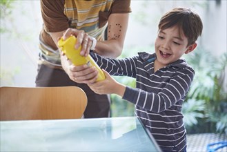 Hispanic boy helping father spray cleaner on table