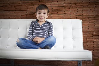 Hispanic boy sitting cross-legged on sofa