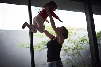 Playful Hispanic mother lifting daughter