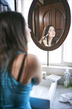 Hispanic woman using makeup brush in mirror