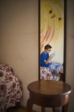 Reflection in mirror of Hispanic boy reading book on bed