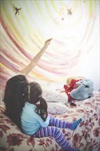 Hispanic mother and daughter on bed looking at mural on wall