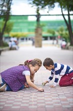 Hispanic brother and sister drawing on sidewalk with chalk