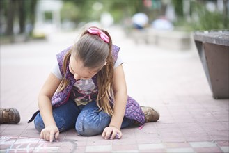 Hispanic girl drawing with chalk on sidewalk