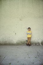 Serious Hispanic boy leaning on concrete wall