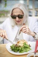 Older Caucasian woman cutting food on plate