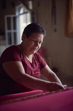 Hispanic woman weaving fabric on loom