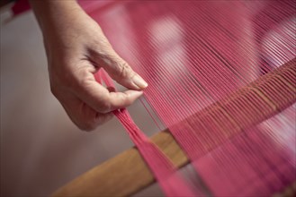 Hand of Hispanic woman weaving fabric on loom