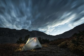 Illuminated camping tent under cloudy sky
