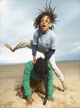 Mixed Race boy jumping over father on beach