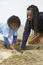 African father and son digging in sand