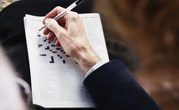 Close up of senior man's hand with pen on crossword puzzle