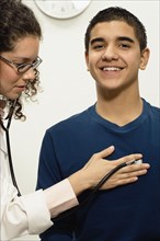 Female doctor checking young male patient with stethoscope