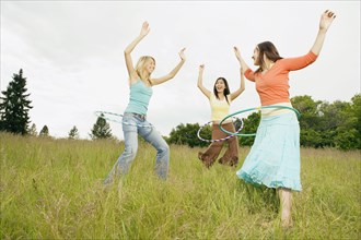 Three young women playing with plastic hoops in meadow