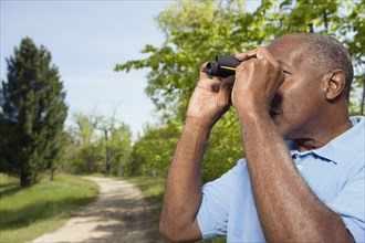 Senior African man using binoculars in park