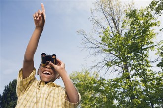 African boy using binoculars and pointing in park