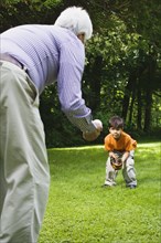 Hispanic boy playing catch with grandfather in park