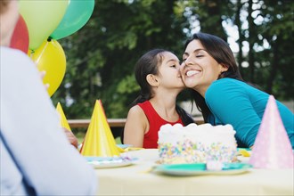 Hispanic girl kissing mother's cheek at birthday party