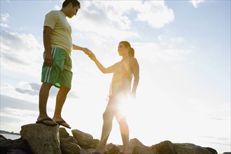 Hispanic couple holding hands on rocks at beach