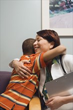 Hispanic female doctor hugging at boy in waiting room