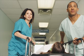 Two nurses wheeling gurney with patient in corridor of hospital