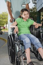 Girl in wheelchair with nurse on sidewalk next to hospital