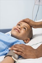 African boy in hospital bed with mother's hand on forehead