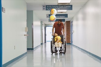African father pushing son in wheelchair down hospital corridor
