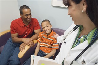 Hispanic female doctor smiling at African father and son in waiting room