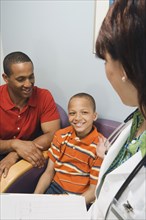 Hispanic female doctor talking to African father and son in waiting room