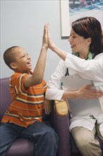 African boy and Hispanic female doctor high-fiving in waiting room