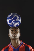 African American man balancing soccer ball on head