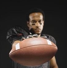 African American male football player holding out football