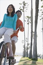 Asian man riding bicycle with girlfriend on handlebars