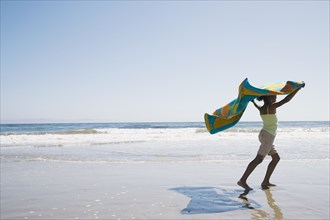 African girl holding beach towel in wind