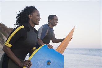 African couple carrying surfboard and boogie board