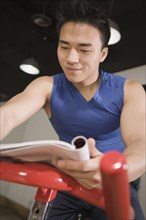 Chinese man reading magazine on exercise bicycle