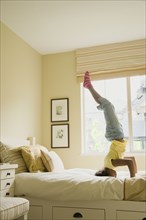African American girl doing headstand on bed