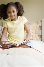 African American girl reading book in bed