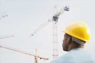 Black construction work in hard-hat looking at crane