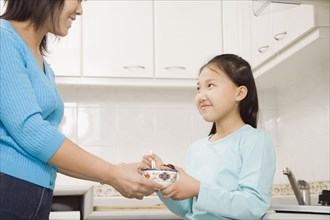 Chinese mother handing daughter bowl of food