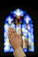 African woman's hands clasped in prayer in front of stained glass window