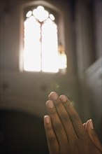 Light from church window shining on hands clasped in prayer