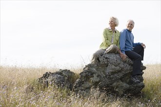 Caucasian couple sitting on rock in field