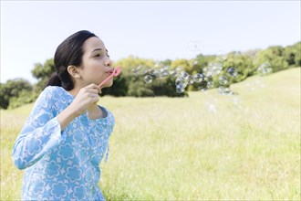 Hispanic girl blowing bubbles in field